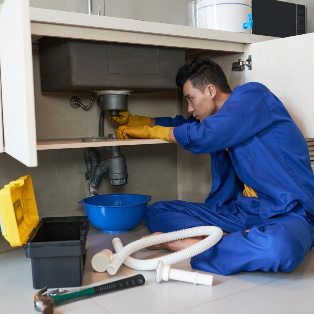 Young Vietnamese plumber checking drain in kitchen