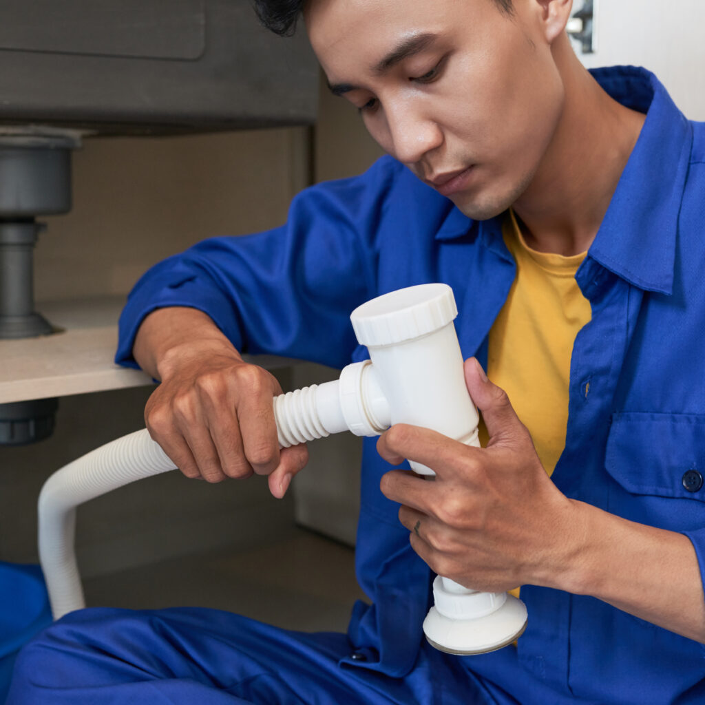 Young professional plumber concentrated on assembling sink pipe